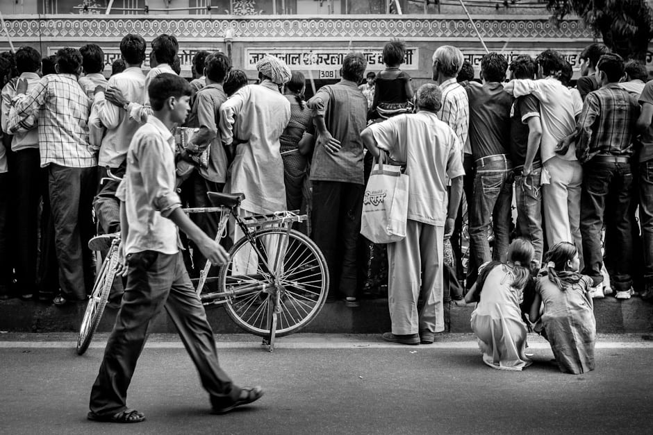 Two young girls watch the Teej Festival parade through the legs of the crowd.